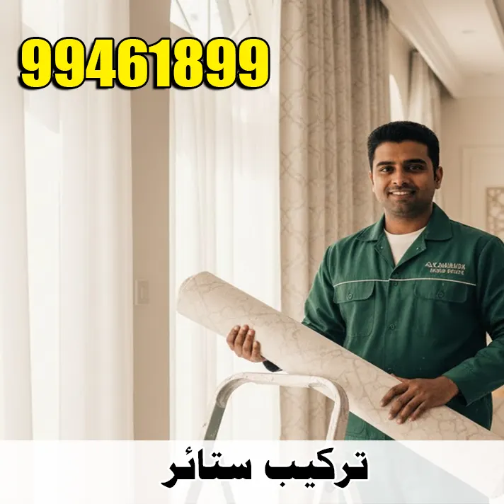 فني تركيب ستائر هندي يرتدي زياً أخضر، يحمل رول ستارة مبتسماً في صالة منزل كويتي.