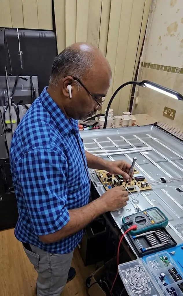 فني تصليح تلفزيونات هندي في الكويت يقوم بفحص بوردة الشاشة داخل الورشة